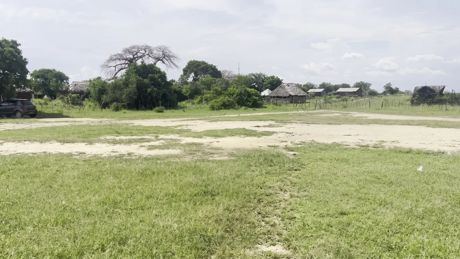 Open plots bordered by mature trees and neighbouring homes near Mambrui, Kilifi County